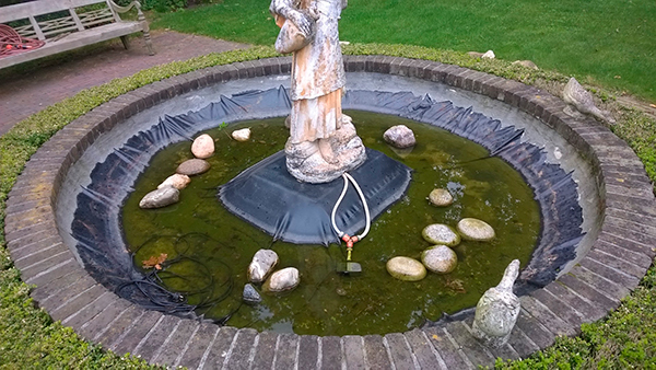 een fontein in de achtertuin van een woning in Elspeet met een wit beeld van van circa anderhalve meter van een meisje die twee waterkannen vasthoudt